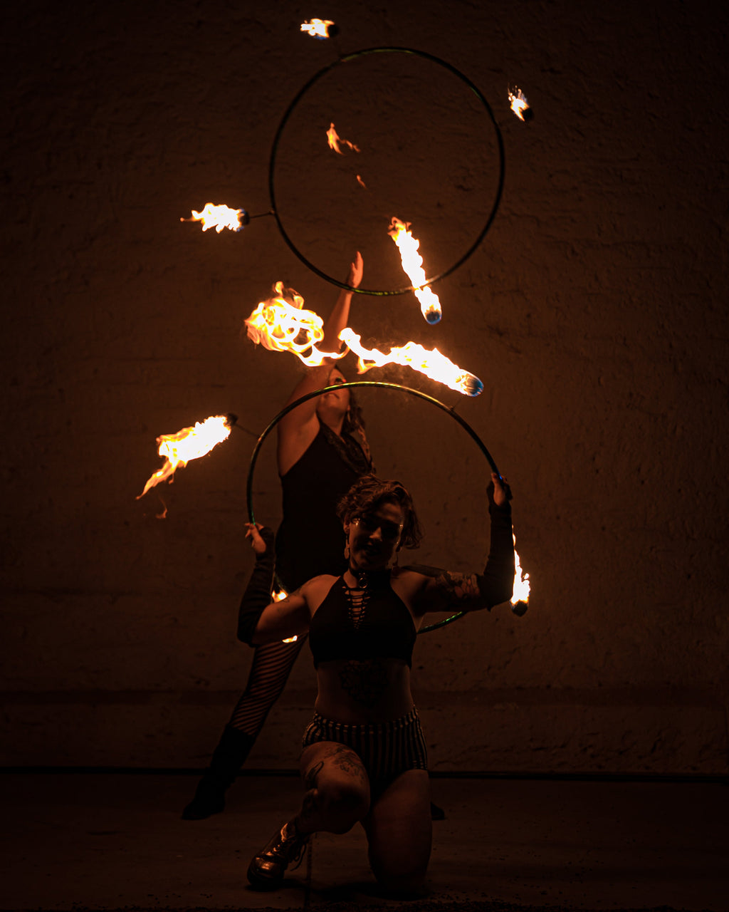 Two fire hoop rings with burning wicks, performer crouching and holding props.