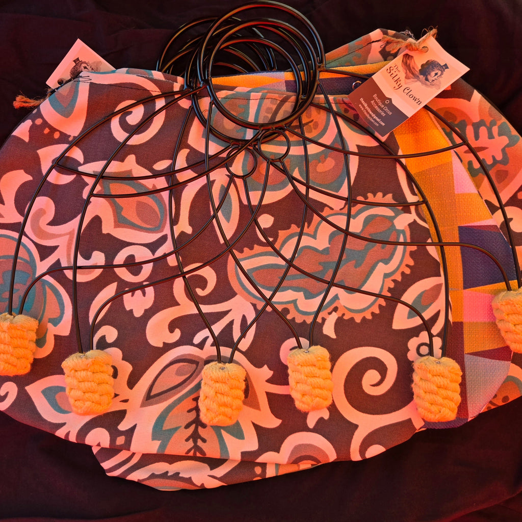 Patterned fan cover with black cord ring stays and orange pom-pom tassels at corners.